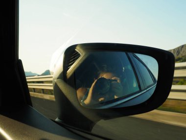 Dikiz aynasının fotoğrafını çeken genç bir kadın.