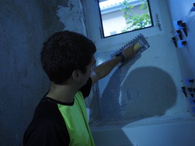 Genç adam bina inşaatında bir aletle çalışıyor.