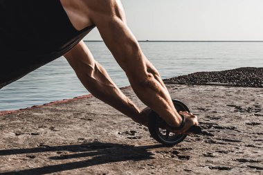 Sportif adam, karın kaslarını güçlendirmek için yaz sabahı denize karşı karın kaslarıyla egzersiz yapıyor. Kaslı erkek elleri