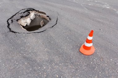 Sokak şehri ve trafik konisi üzerindeki derin subatan. Asfalt otobanında tehlikeli bir delik. Çatallı yol. Kötü inşaat. Hasar