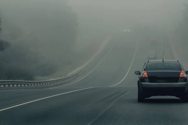 Автомобили в тумане едут по шоссе в опасную погоду. Плохая проходимость и автомобильный трафик на дороге. Транспортные средства в тумане на автостраде — стоковое фото