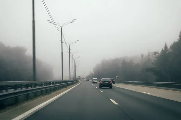 Automobilový provoz na dálnici s bariérou. Mlha nebo opar na silnici, nebezpečné zatažené počasí pro řízení vozidla. Dálnice v lese v mlze — Stock fotografie