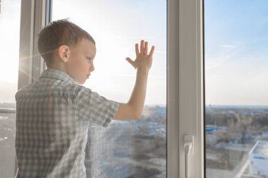 Çocuk ayağa kalktı ve pencereden dışarı baktı. Yürümeye başlayan çocuğun üzüntüsü. Çocukların apartman penceresinden düşme tehlikesi. Tecrit