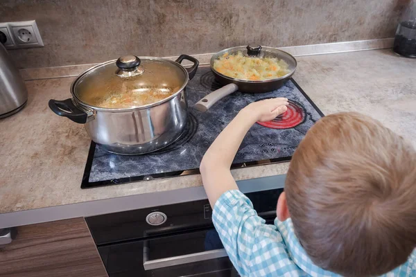 Toddler boy touches hot stove in kitchen. Accident at home with children.  Child pulls a hand to a scorching pan Stock Photo