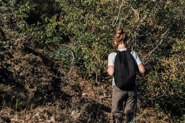 Girl tourist with backpack is walking along forest trail. Wild adventure trekking in nature. Traveler on stroll in remote location