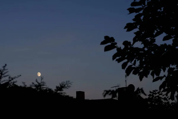 夜晚月亮挂在乡间房屋的屋顶上 — 图库照片