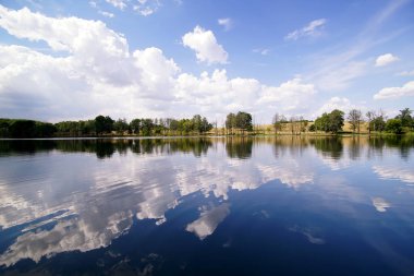 Gölün sakin sularında bulutlarla kaplı gökyüzünün yansıması.