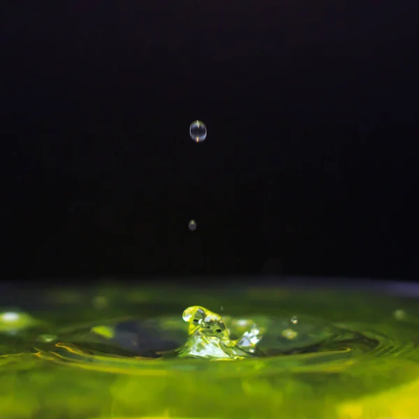 Yellow color water drop falling in water, freezing the moment