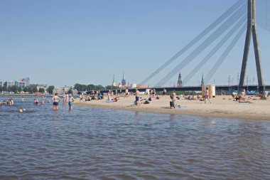 Riga, Letonya - Haziran 2020: Şehir plajı ziyaretçileri nehir suyunun tadını çıkarıyor ve güneşli bir günde güneşleniyor.