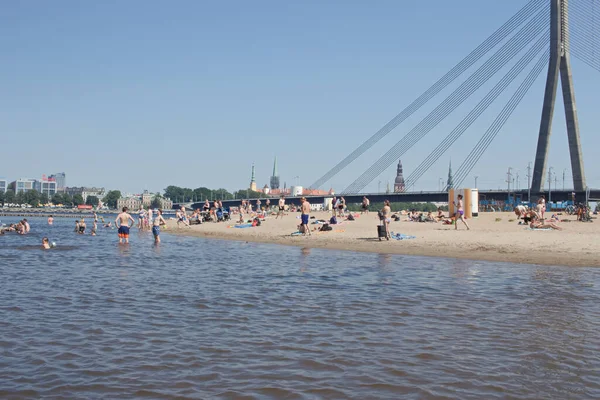 Riga, Letonya - Haziran 2020: Şehir plajı ziyaretçileri nehir suyunun tadını çıkarıyor ve güneşli bir günde güneşleniyor.