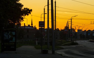 Riga, Letonya - 17 Temmuz 2020: Şehir sokağı, gün doğumunda otobüs durağı, elektrik hatları