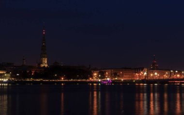 Riga, Letonya - 24 Eylül 2020: gece başkent manzarası. Karanlık gökyüzü, aydınlık bina ve şehir nehri