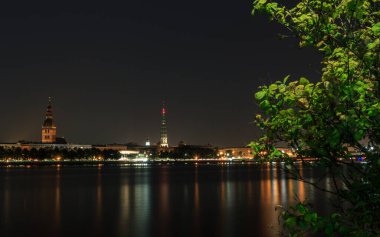 Riga, Letonya - 24 Eylül 2020: gece başkent manzarası. Karanlık gökyüzü, aydınlık bina ve şehir nehri