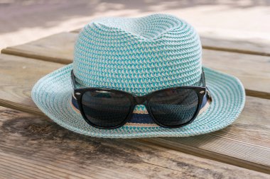 Ahşap yüzeyde güzel mavi bir şapka ve güneş gözlüğü var..