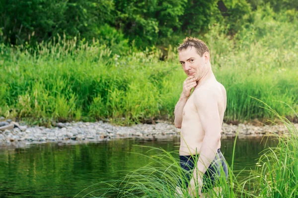 川のほとりで野生のタイガを背景に 川の中に立つ若い男は 面白いと奇妙な顔をしている — ストック写真