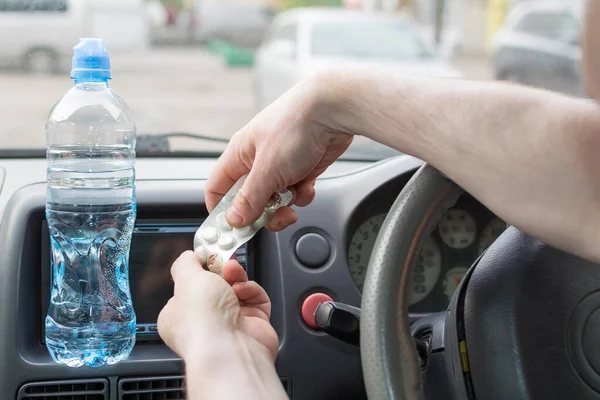 A man in a car opens a package of pills. Tablets and a bottle of water in the auto.