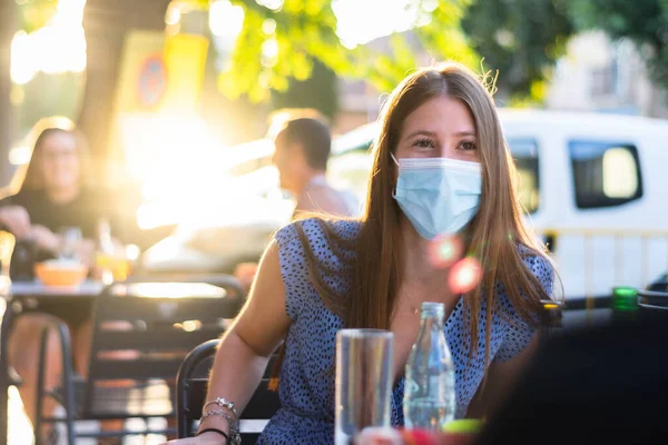 Spain Madrid. Caucasian woman wearing sanitary mask. Reopen pubs and club after quarantine coronavirus Covid-19. Woman drinking beer. People smiling in masks. Summer 2020 new normal