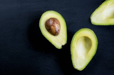 Siyah masanın üzerinde dilimlenmiş avokado üst görüntüsü. Sağlıklı gıda konsepti.