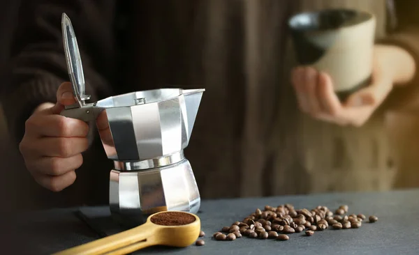 Nő kezében hagyományos moka pot kávéfőző készen áll, hogy öntsön friss kávét a kis csésze. Kávébab és őrölt kávé a háttérben. Stock Kép