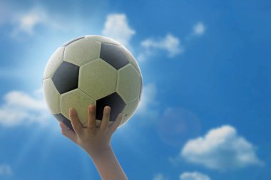 Çocuk futbol topunu başının üzerinde tutuyor. Gökyüzünün parlak ve parlak arka planında kırpma yolu ile.