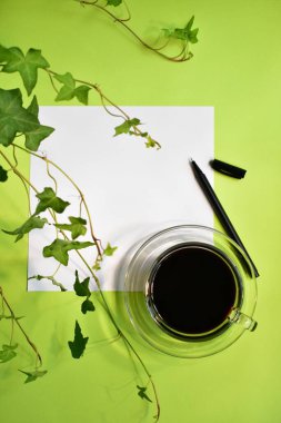 Yeşil iş yeri, koyu kahve fincanı olan yeşil ofis masası, pastel yeşil arka plan, taze, yeni hayat, huzur, çevre dostu, üst manzara, düz yatak, boş not, beyaz kalem, boş kalem.