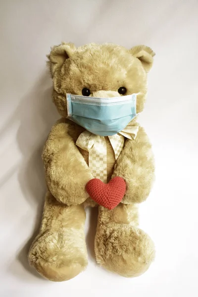 Cute brown bear with blue medical mask in white background, red heart. Teddy bear wearing face mask protective for spreading of disease virus CoV-2 Corona virus Disease quarantine, stay safe