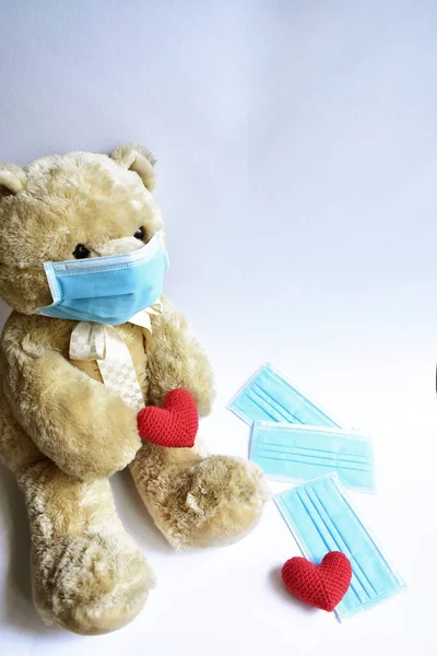 Cute brown bear with blue medical mask in white background, red heart. Teddy bear wearing face mask protective for spreading of disease virus CoV-2 Corona virus Disease quarantine, stay safe