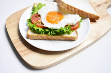 Sandviçli sağlıklı kahvaltı yemeği, kızarmış yumurta, domates dilimi, salata, nane yaprağı, ahşap kesim tahtası, beyaz arka plan, güneşli, abur cubur, kilo verme, organik, basitlik, vegan, burger, düşük yağ oranı, fitness menüsü, kapatın.