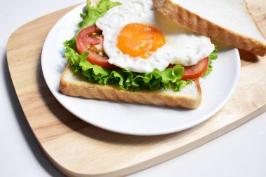 Sandviçli sağlıklı kahvaltı yemeği, kızarmış yumurta, domates dilimi, salata, nane yaprağı, ahşap kesim tahtası, beyaz arka plan, güneşli, abur cubur, kilo verme, organik, basitlik, vegan, burger, düşük yağ oranı, fitness menüsü, kapatın.