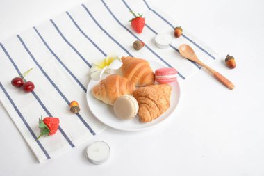 Düz yatak, üst manzara, beyaz arka planda yiyecek ve içecek, kruvasanlarla sağlıklı kahvaltı, Fransız makarnası, çilek, kuru meşe palamudu, kaşık, pembe orkide, kiraz, tatlı, ev yapımı, yemek, vegan