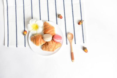 Düz yatış, üst manzara, beyaz arka planda yiyecek ve içecek, kruvasanlarla sağlıklı kahvaltı, Fransız makarnası, çilek, kuru meşe palamudu, kaşık, kiraz, beyaz Fragipan çiçeği.