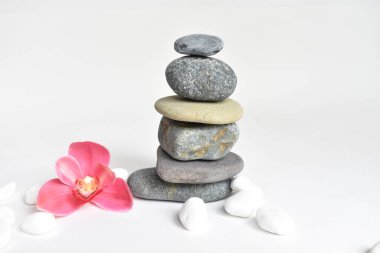 Beyaz arka planda izole edilmiş taş yığınları ve pembe orkide çiçeği. Çakıl taşı kulesi. Denge ve uyum kavramı. Sakin ve ruh, spa taşları ve zen, barış, meditasyon, manevi ve soyut