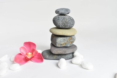 Beyaz arka planda izole edilmiş taş yığınları ve pembe orkide çiçeği. Çakıl taşı kulesi. Denge ve uyum kavramı. Sakin ve ruh, spa taşları ve zen, barış, meditasyon, manevi ve soyut
