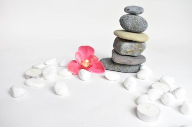 Beyaz arka planda izole edilmiş taş yığınları ve pembe orkide çiçeği. Çakıl taşı kulesi. Denge ve uyum kavramı. Sakin ve ruh, spa taşları ve zen, barış, meditasyon, manevi ve soyut