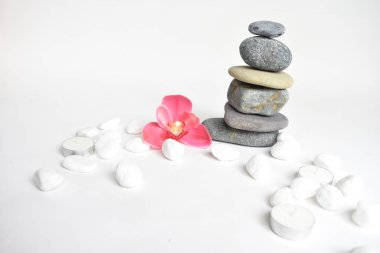 Beyaz arka planda izole edilmiş taş yığınları ve pembe orkide çiçeği. Çakıl taşı kulesi. Denge ve uyum kavramı. Sakin ve ruh, spa taşları ve zen, barış, meditasyon, manevi ve soyut