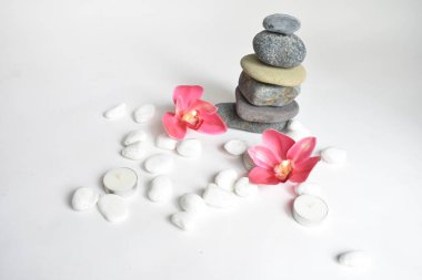 Beyaz arka planda izole edilmiş taş yığınları ve pembe orkide çiçeği. Çakıl taşı kulesi. Denge ve uyum kavramı. Sakin ve ruh, spa taşları ve zen, barış, meditasyon, manevi ve soyut