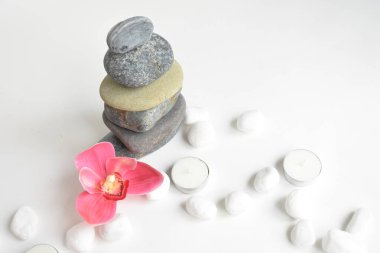 Beyaz arka planda izole edilmiş taş yığınları ve pembe orkide çiçeği. Çakıl taşı kulesi. Denge ve uyum kavramı. Sakin ve ruh, spa taşları ve zen, barış, meditasyon, manevi ve soyut