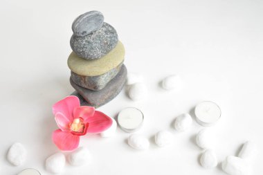 Beyaz arka planda izole edilmiş taş yığınları ve pembe orkide çiçeği. Çakıl taşı kulesi. Denge ve uyum kavramı. Sakin ve ruh, spa taşları ve zen, barış, meditasyon, manevi ve soyut