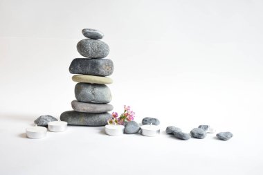 Beyaz arka planda izole edilmiş taş yığınları ve pembe balmumu çiçekler. Çakıl taşı kulesi. Denge ve uyum kavramı. Sakin ve ruh, spa taşları ve zen, barış, meditasyon, manevi ve soyut