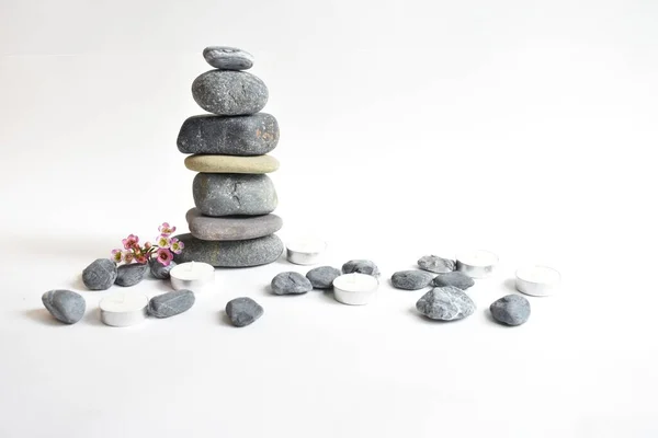 Stack stones isolated in white background and pink wax flowers. Pebbles tower. Concept of balance and harmony. Calm and spirit, spa stones and zen, peace, meditation, spiritual, abstract