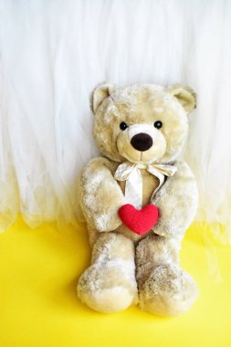 Sarı ve beyaz şifonlu kırmızı bir kalp taşıyan sevimli oyuncak oyuncak, rahatla, yaz tatili, çocuk oyuncağı, çocukluk anısı, aşk, sevgililer günü ayısı