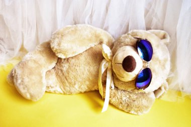 Tatlı oyuncak ayıcık kumsalda yatıyor, sarı ve beyaz şifon arka plan, rahatla, yaz tatili, çocuk oyuncağı, çocukluk anısı