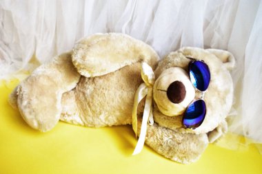 Tatlı oyuncak ayıcık kumsalda yatıyor, sarı ve beyaz şifon arka plan, rahatla, yaz tatili, çocuk oyuncağı, çocukluk anısı