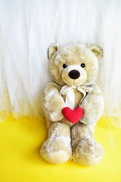 Cute teddy bear soft toy holding a red heart in yellow and white chiffon background, relax, summer holiday, kid toy, childhood memory, love, valentine bear