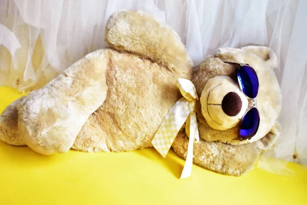 Cute teddy bear soft toy lying on the beach, yellow and white chiffon background, relax, summer holiday, kid toy, childhood memory