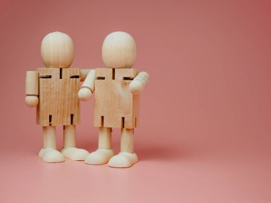 Oturan ve ayakta duran 2 tahta bebek pembe arka planda konuşuyorlar. Tahta bebeklerden sosyal temas kavramı..