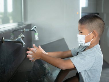 Maske takan bir çocuk umumi tuvaletlerde ellerini yıkıyor.