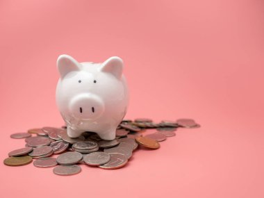 Beyaz domuz kumbarası pembe arka plandaki bozuk para yığınının üstüne yerleştirilmiş. Para biriktirme kavramı.
