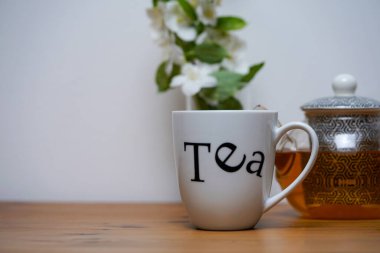 Bir fincan yasemin çayı, çaydanlık ve arka planda beyaz yasemin çiçekleri. Hepsi ahşap masaya yerleştirilmiş.. 