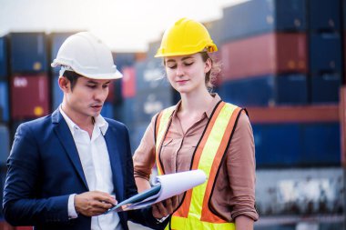 Mühendis konteynır deposunda sabit kasklı bir kargo taşıyor ve kargo nakliye gemisinden ithalat ve ihracat için konteynır kutusunu kontrol ediyor. Takım çalışması konsepti 